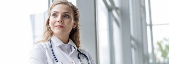 Ärztin steht selbstbewusst mit verschränkten Armen vor einem Fenster