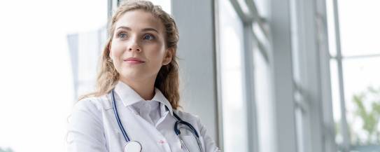 Ärztin steht selbstbewusst mit verschränkten Armen vor einem Fenster
