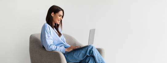 Junge Frau in einem Sessel ließt lächelnd am Laptop