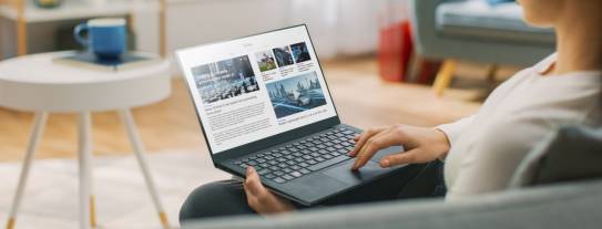 Frau sitzt auf der Couch im Wohnzimmer und scrollt am Laptop