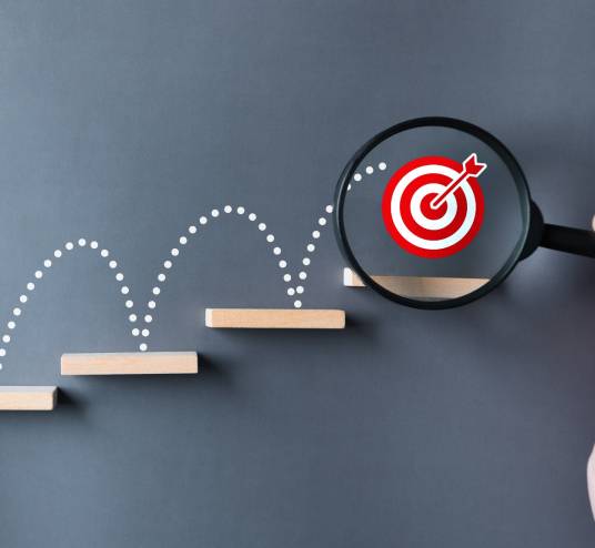 Holztreppchen mit Sprunglinien zum Ziel, das mit einer Lupe vergrößert wird